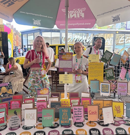 Emma and Ruby smiling and womanning one of our Damn Fine Greetings stands showcasing our colourful sweary and not-so-sweary range of greetings cards and gifts.