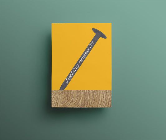Warm yellow greetings card with a nail hammered into a piece of wood. The nail has the words 'Fucking Nailed It!' on the side.
